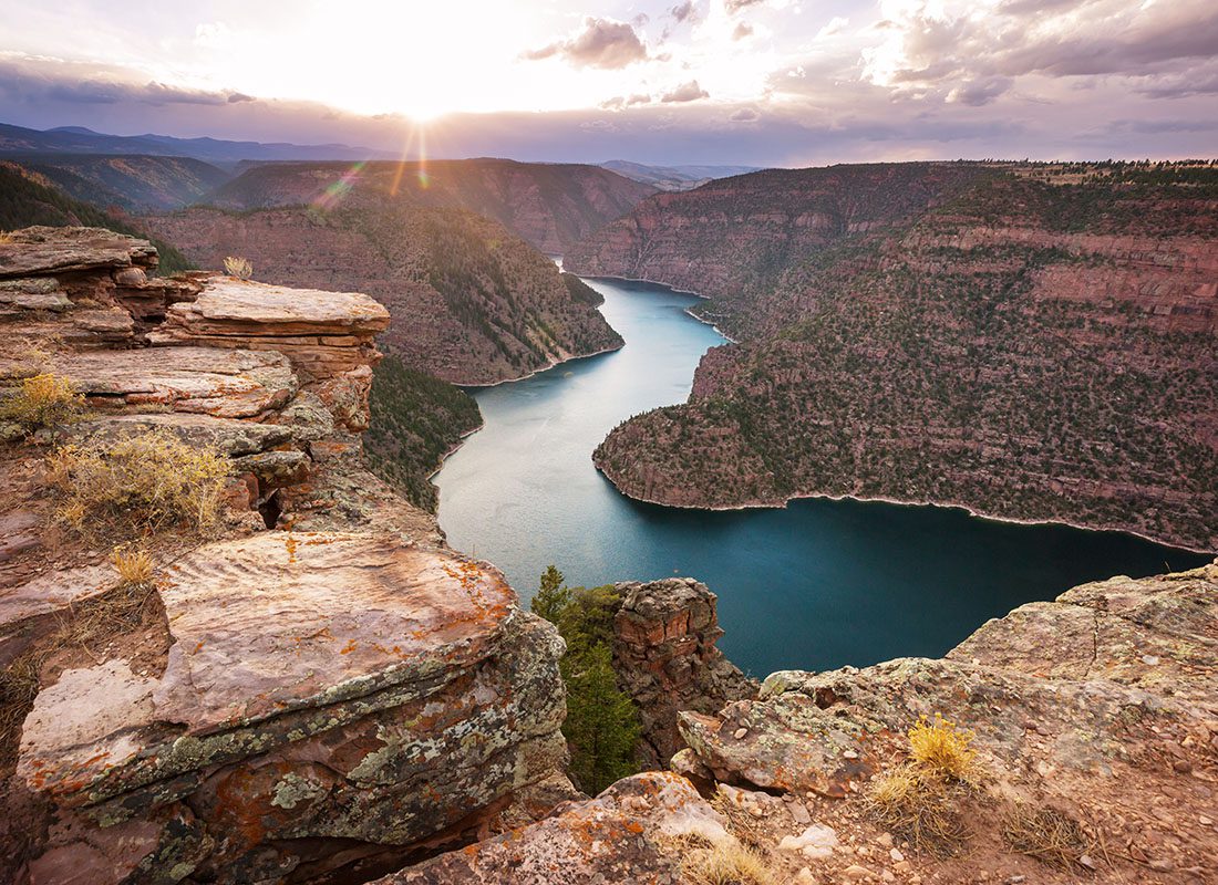 About Our Agency - View of the Colorado River Surrounded by Stone Formations at Sunset with a Colorful Sky in a Canyon