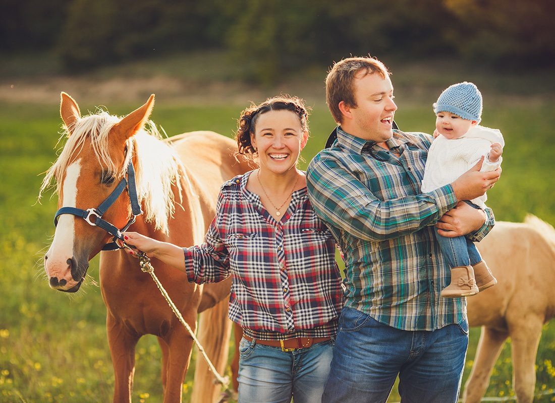 Personal Insurance - Portrait of a Happy Parents Standing Outside on the Green Grass with Their Horse While Holding Their Baby Girl