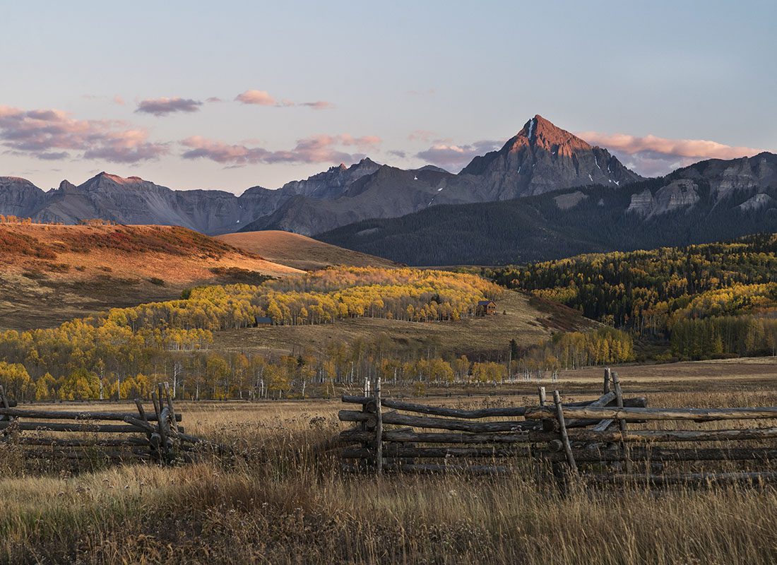 Service Center - Scenic Landscape of Tall Grass in a Meadow with an Old Wooden Fence and Green Trees and Mountains in the Background at Sunset in Colorado